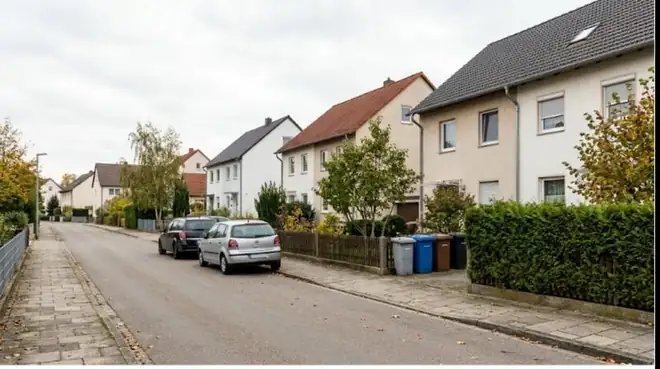 Wohnstraße in einer deutschen Kleinstadt mit Einfamilienhäusern und Doppelhaushälften, Hecken, Gehweg und parkenden Autos.